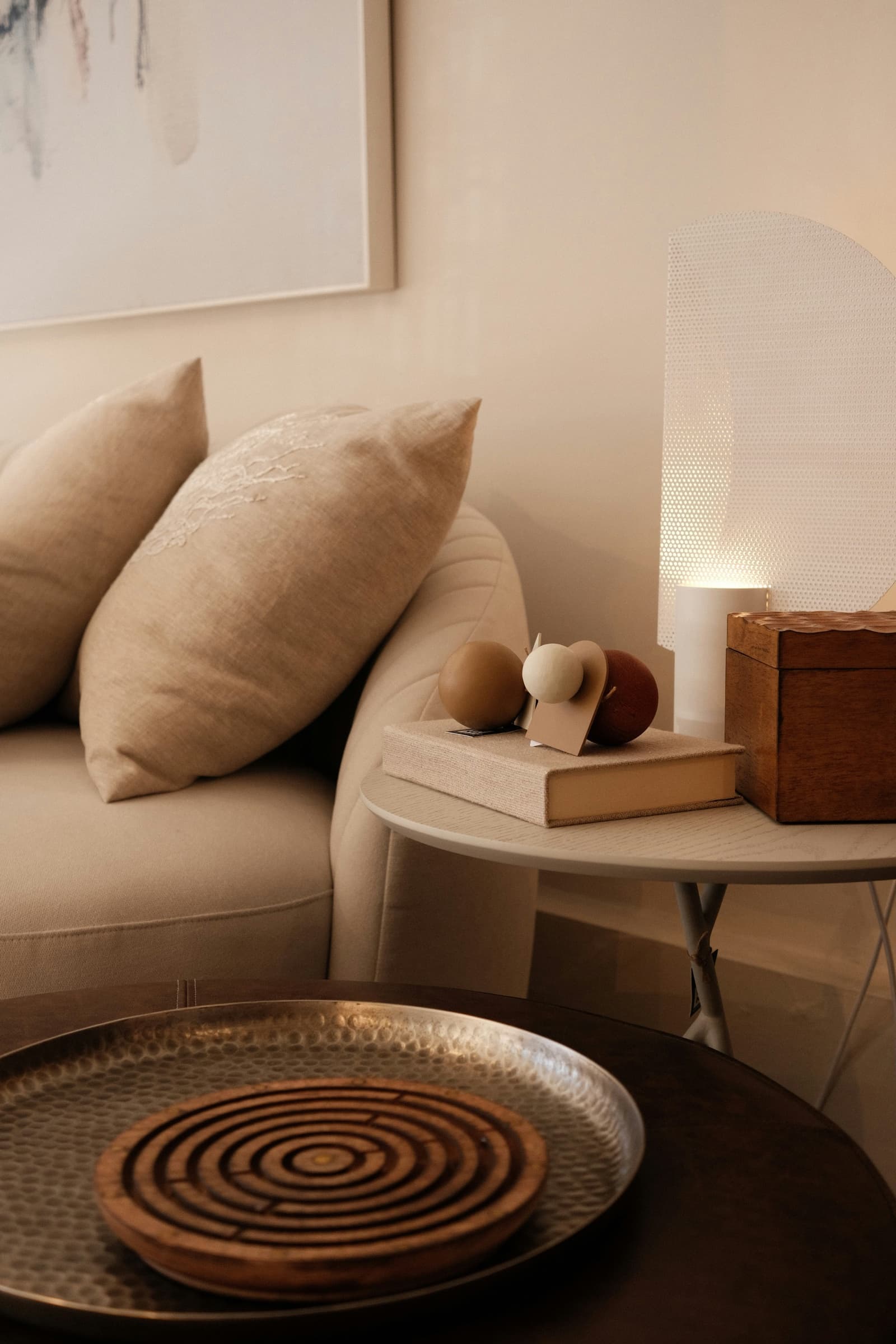 A quiet morning corner with a linen sofa, a side table holding a book and sculptural objects, and a warm glowing lamp
