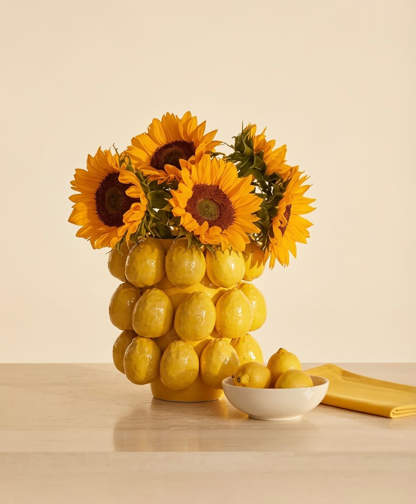 A glossy yellow ceramic planter shaped like clustered lemons holding sunflowers