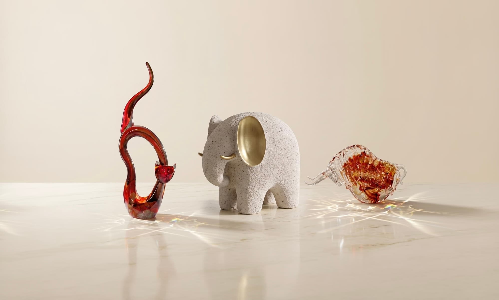 A speckled stone elephant sculpture with brass ears beside amber glass figures on marble